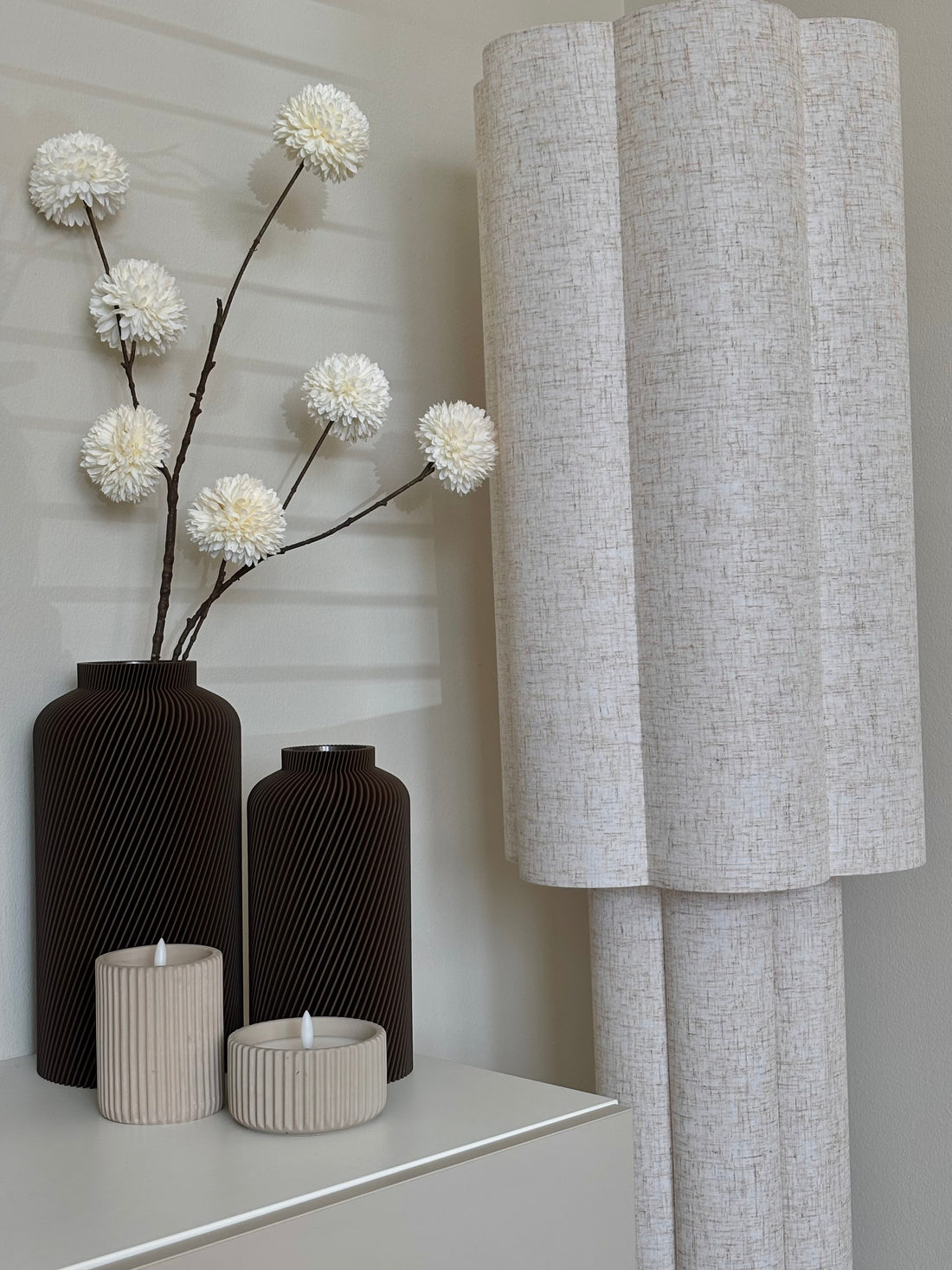 Two brown Silo vases, a tall one with long white flower stems, beside ribbed candle holders